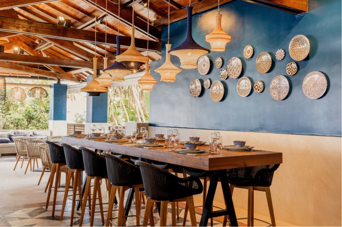 Bistro-style table with ten chairs at Club Med Yasmina, adorned with decorative plates on the wall and a wooden roof. Bistro-style table with ten chairs at Club Med Yasmina, adorned with decorative plates on the wall and a wooden roof.