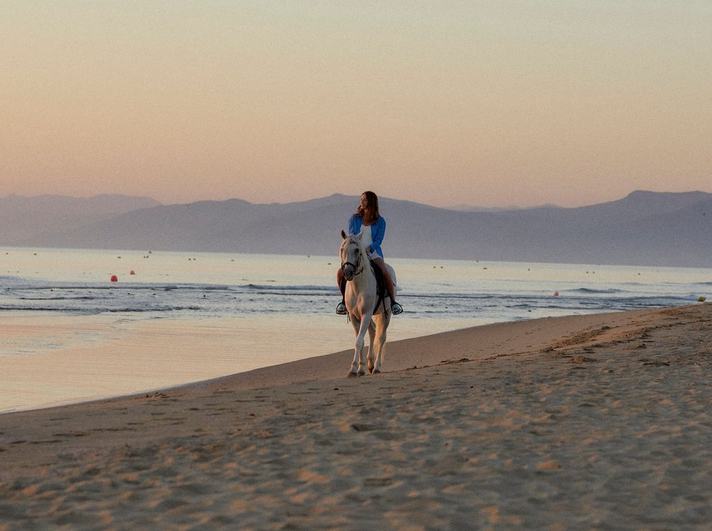 Woman riding a horse along the beach at Club Med Yasmina, with a stunning sunset in the background. Woman riding a horse along the beach at Club Med Yasmina, with a stunning sunset in the background.